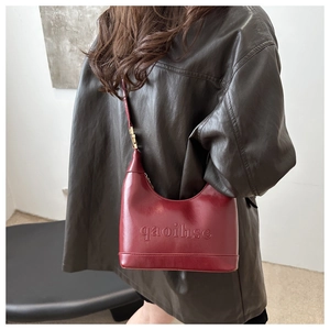 Detail of red glossy leather crescent bag with embossed letter texture on the side