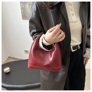 Detail of burgundy leather handbag featuring embossed lettering and a glossy finish