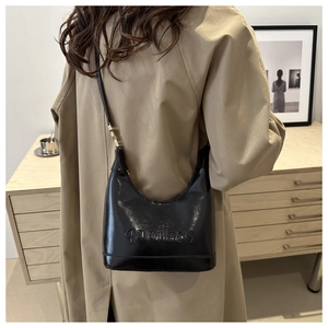Close-up of black glossy patent leather shoulder bag featuring embossed letter details