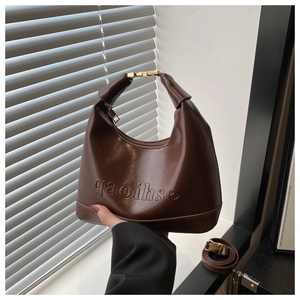Detail of dark brown dumpling bag featuring logo embossing and gold metallic hardware
