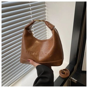 Detail of brown faux leather crescent bag with embossed text and gold metallic buckle