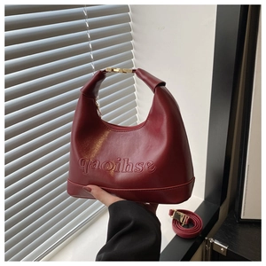 Detail of burgundy PU leather square bag with embossed lettering and gold metal clasp
