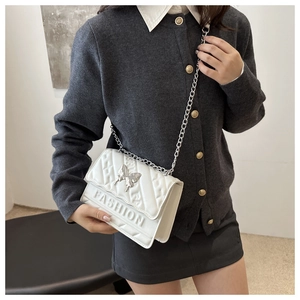 Detail of white quilted crossbody bag featuring metal butterfly and silver chain strap