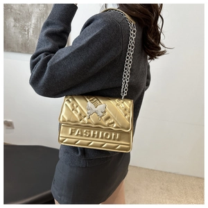 Detail of gold crossbody bag with silver butterfly clasp and FASHION embossed texture