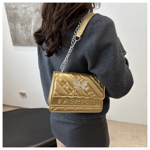 Detail of gold quilted shoulder bag with metal butterfly buckle and silver chain strap