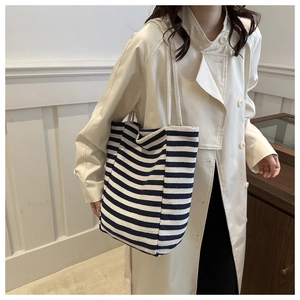 Détail d'un sac cabas en toile rayé bleu et blanc avec anses en corde porté par un mannequin
