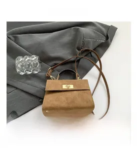 Detail view of khaki suede handbag featuring golden twist-lock closure and metal studs