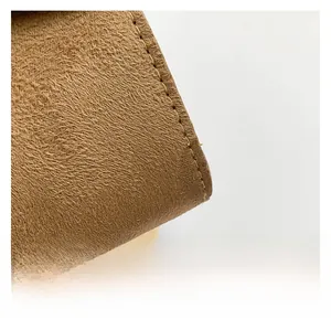 Close-up of premium brown suede leather texture with detailed stitching on crossbody bag