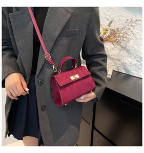 Detail of burgundy suede square crossbody bag with metallic twist lock on grey blazer
