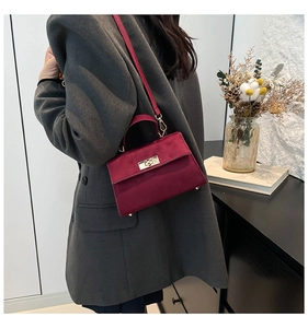 Detail of burgundy velvet handbag featuring a gold metal twist lock on a gray suit outfit