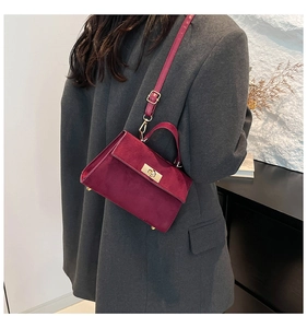 Detail of burgundy velvet mini bag with gold lock and sleek shoulder strap worn by a model