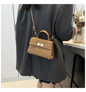 Brown suede square bag worn crossbody on a grey blazer, showing retro metal lock detail