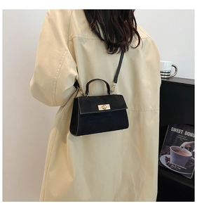 Detail of a vintage black suede crossbody bag with gold lock worn with a beige trench coat