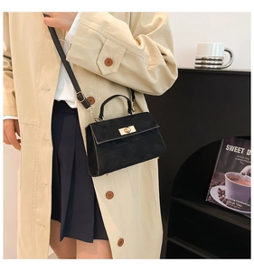 Detail of black crossbody bag with gold twist lock on a beige trench coat