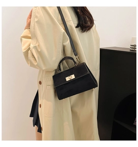 Detailed view of a black suede handbag with gold clasp worn by a model in a beige coat