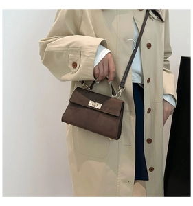 Detail of dark brown suede crossbody bag featuring a classic gold metal twist lock closure
