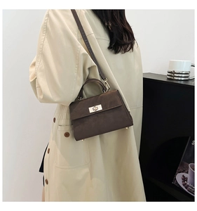 Detail of dark brown suede mini handbag featuring a golden clasp and a slender shoulder strap