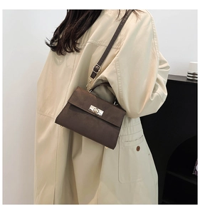 Dark brown suede crossbody bag with metal twist lock shown on beige trench coat