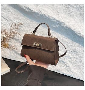 Detail view of dark brown suede crossbody bag with gold metal twist lock and matte texture