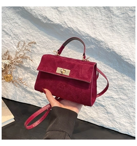 Close-up of burgundy suede crossbody bag with golden twist lock and top handle