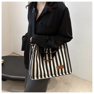 Detail of striped canvas tote bag with brown leather FASHION label and crossbody strap