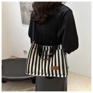 Rear view of model wearing a medium striped canvas tote bag with leather logo tag