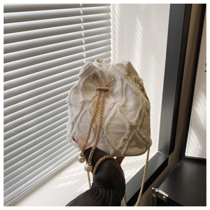 Detailed view of white denim bucket bag featuring frayed lattice texture and pearl chain