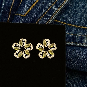 Close-up of olive green zircon flower earrings with gold plating on denim background