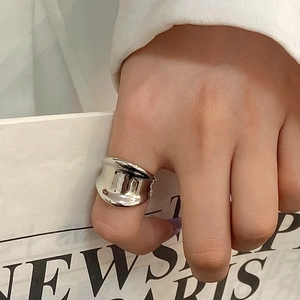 Close-up of a minimalist silver wide ring with an irregular wavy surface on a thumb