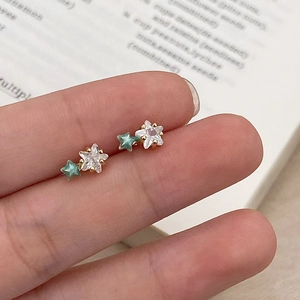 Close-up of gold-plated star studs with white zircon and teal enamel on a book