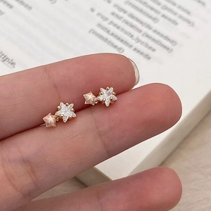 Macro detail of star stud earrings with crystals held to show actual dainty size