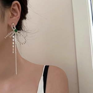 Macro view of crystal bow earrings featuring long silver tassels and green bead accents