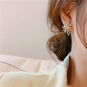 Macro shot of gold firework starburst earrings with sparkling crystals worn by model