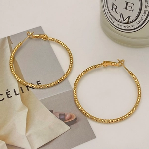 Detail of gold circular hoop earrings with fine beaded texture and polished finish