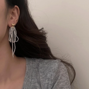 Close-up of handmade beaded tassel earrings with gold heart studs on a female model