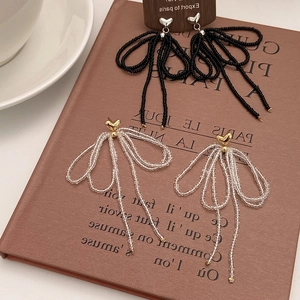 Close-up of handmade beaded bow earrings with heart studs and long hanging tassels