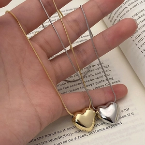 Polished gold and silver heart pendant necklaces with sleek snake chains on a book
