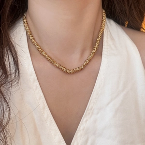 Detailed view of a gold beaded necklace with multiple metal rings on a white V-neck top