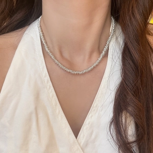 Close-up of a silver beaded necklace featuring a multi-layered textured metal ring design