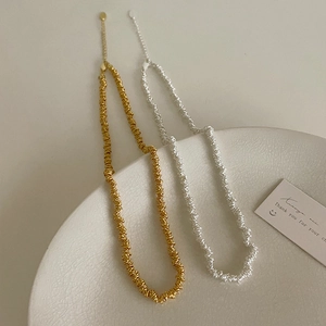 Macro detail of textured gold and silver spiral bead necklaces on white ceramic tray
