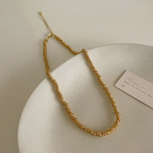 Detail of gold beaded collar necklace with spiral texture on a white ceramic plate