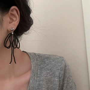 Handcrafted black beaded bow tassel earrings with a silver heart stud on model