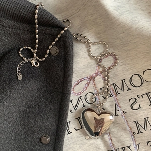Collier chic à perles argentées avec grand pendentif cœur 3D sur fond en tissu neutre