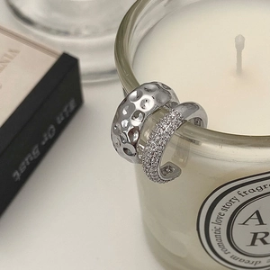 Detail of silver ear cuffs set with hammered texture and pave cubic zirconia on a white candle