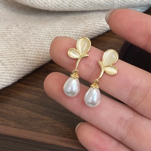 Detail of gold butterfly earrings with cat eye stones and teardrop pearl charms