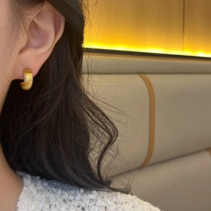 Close-up of matte gold geometric C-shaped chunky hoop earring worn by a model