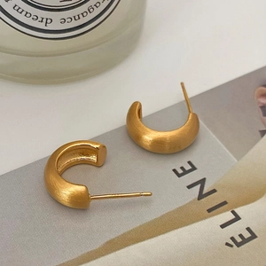 Detail of matte brushed gold C-shaped earrings displayed on a minimalist background
