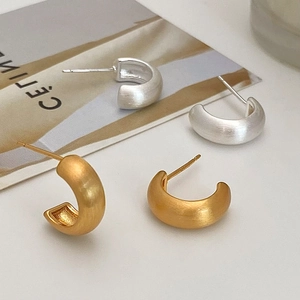 Macro detail of C-shaped semi-circle earrings with elegant matte brushed metal texture