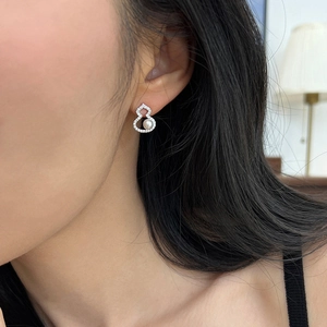 Nahaufnahme eines silbernen Flaschenkürbis-Ohrrings mit Zirkonia und Perle am Ohr