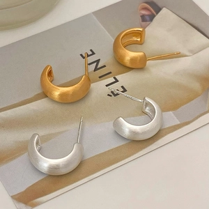 Close-up of matte brushed C-shaped hoop earrings in gold and silver metal finishes
